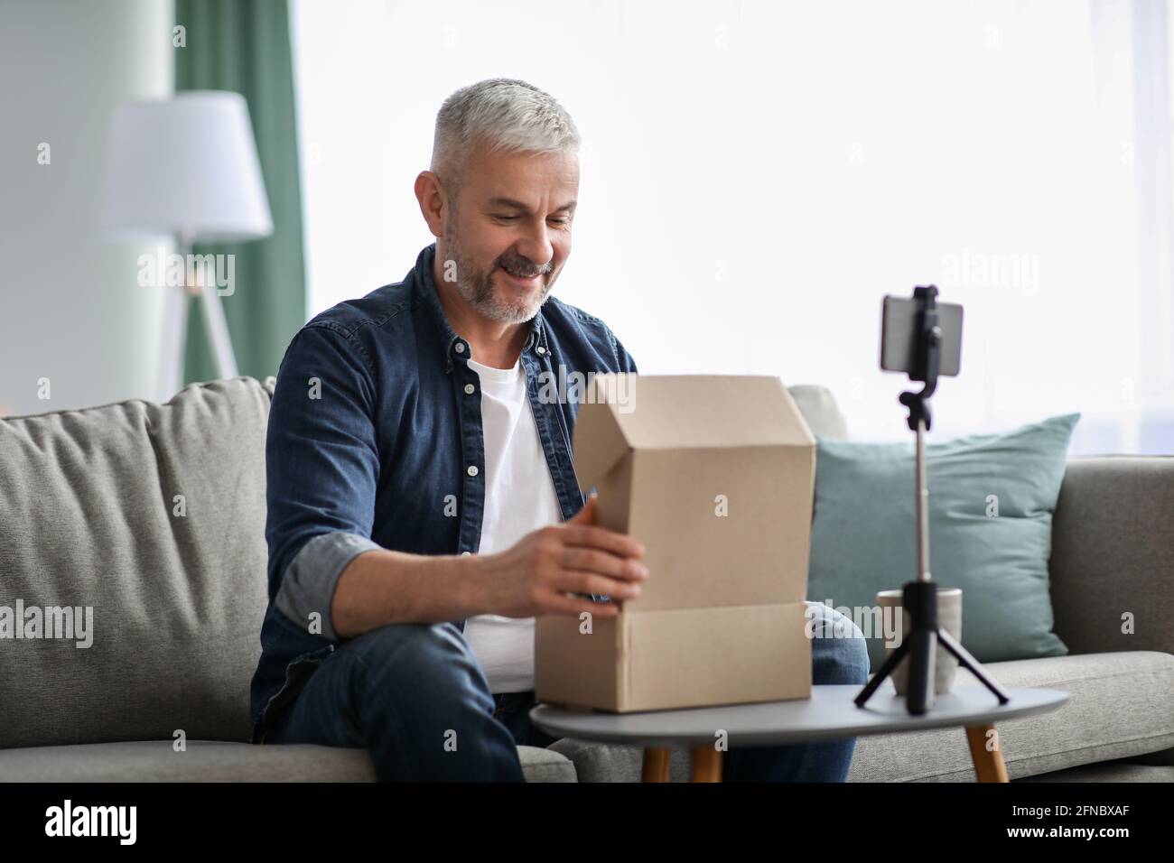 Happy senior man blogger broadcasting while opening delivery box Stock Photo