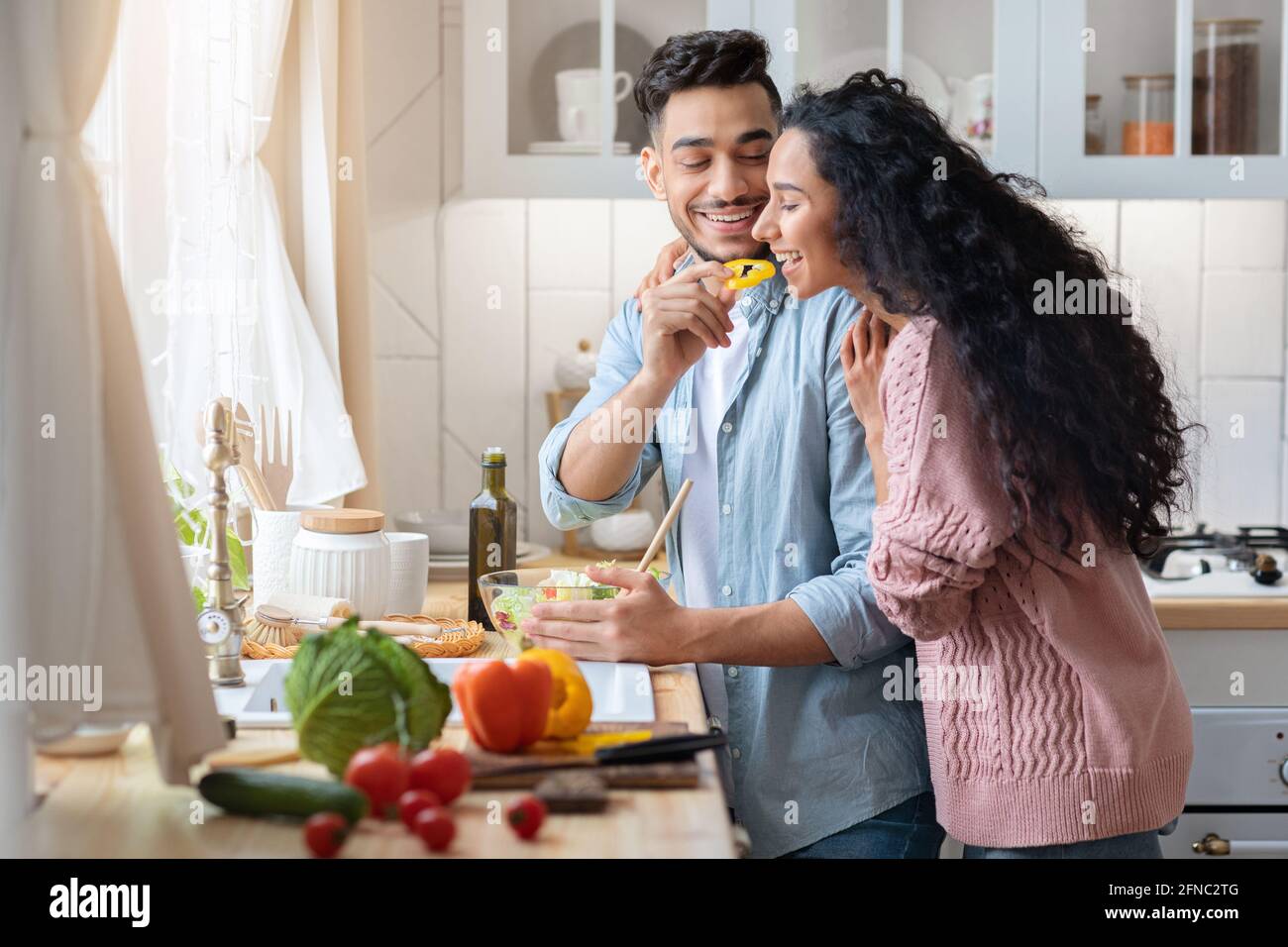 Young Arab Woman Tasting Food While Cooking With Husband In Kitchen Together Stock Photo