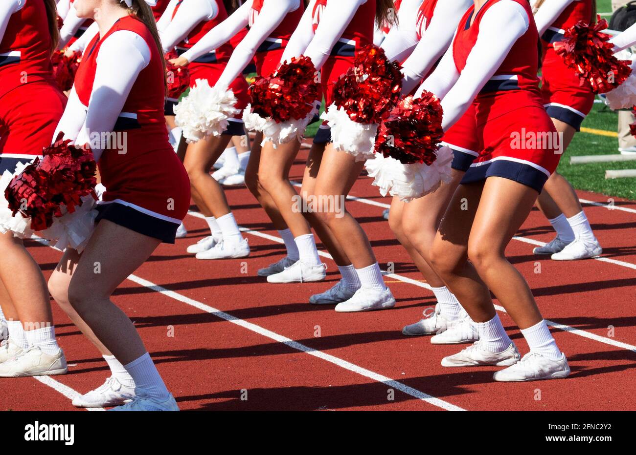 High school cheerleaders in red and white uniforms cheering to the fans during a football game. Stock Photo