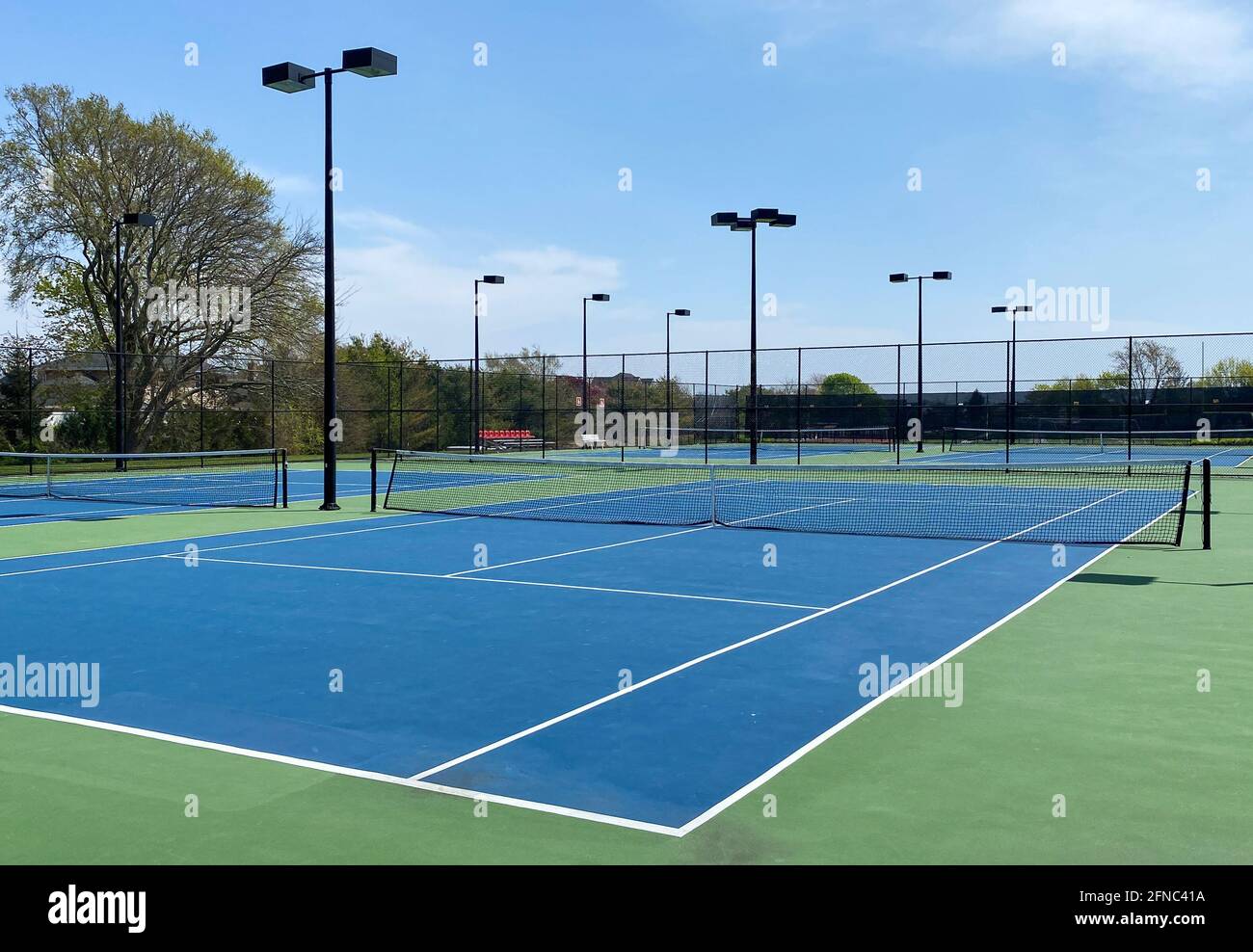 An empty tennis court with a blue and green surface and lights fenced in at a local school. Stock Photo