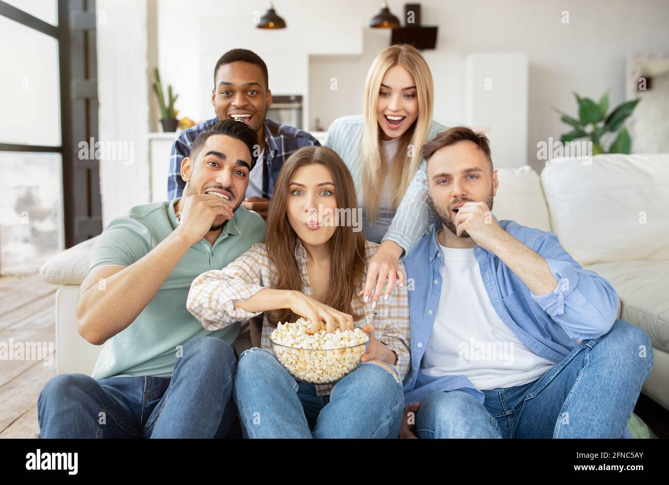 Group of multiracial friends watching TV, eating popcorn, having fun