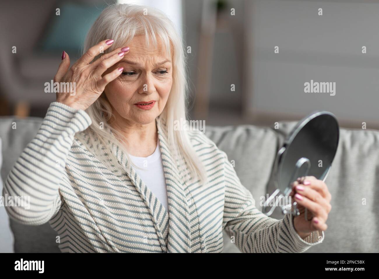 Adult woman checking her face in mirror, touching face Stock Photo