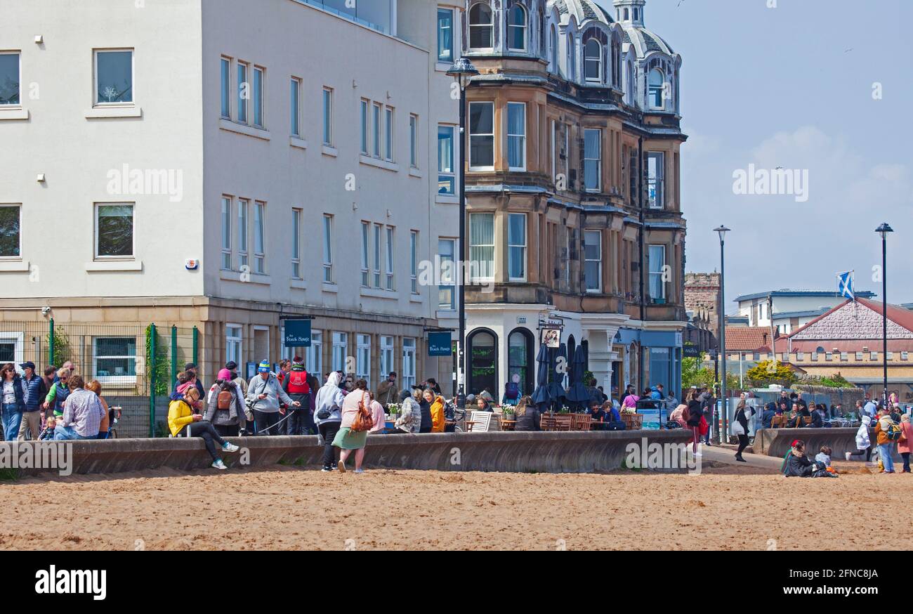 Portobello, Edinburgh, Scotland, UK weather. 16th May 2021. Bright blustery afternoon with temperature of 12 degrees at the reasonably busy seaside. Pictured: People sitting and standing outside The Beach House cafe and takeaway. Credit: Arch White/Alamy Live News. Stock Photo