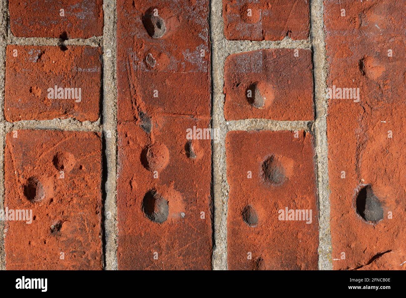 These circular holes in the red bricks have been made by people twisting coins against the wall while waiting to get into the Bath House. Stock Photo