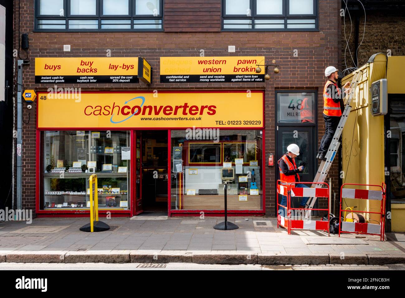 An exterior view of Cash Converters pawn shop on Mill Road.  Electricians in hard hats work nearby. Stock Photo