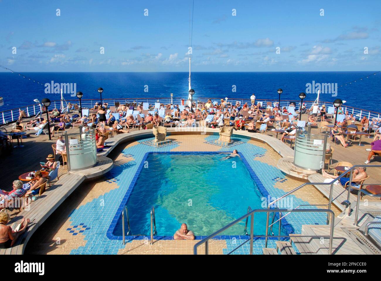 Crowd of passengers sitting around the swimming pool on a cruise ship in the Caribbean Stock Photo