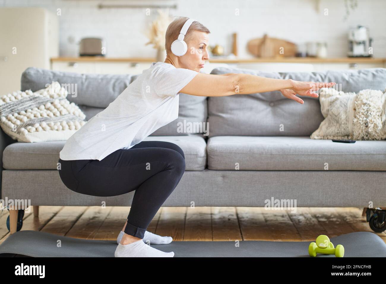 Senior woman stretching, online training in living room. Balancing yoga exercise. Exercising for emotional and spiritual health. Well-being, wellness for retired female. Domestic yoga practice Stock Photo