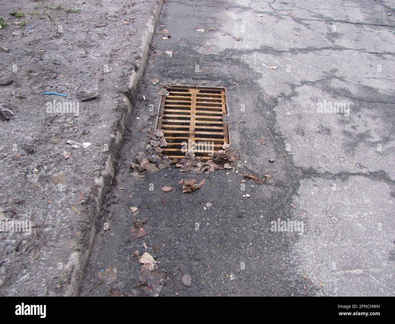 Rusty storm drain grate in cracked asphalt Stock Photo