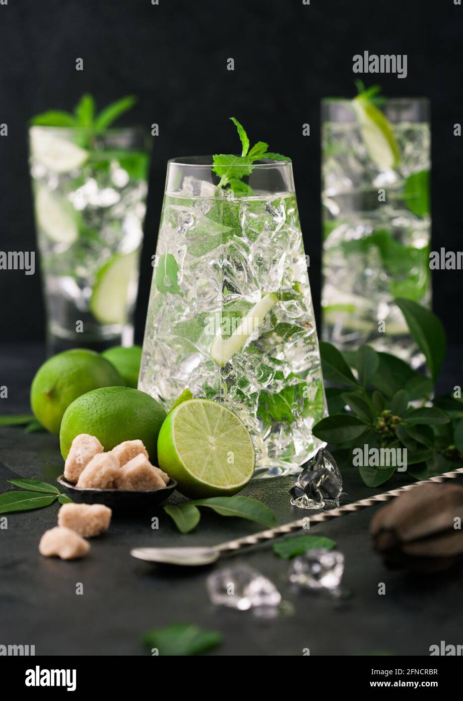 Glasses of Mojito cocktail with ice cubes,mint and lime on black board with spoon and fresh limes with cane sugar. Best party drink.Sparkling mint wat Stock Photo