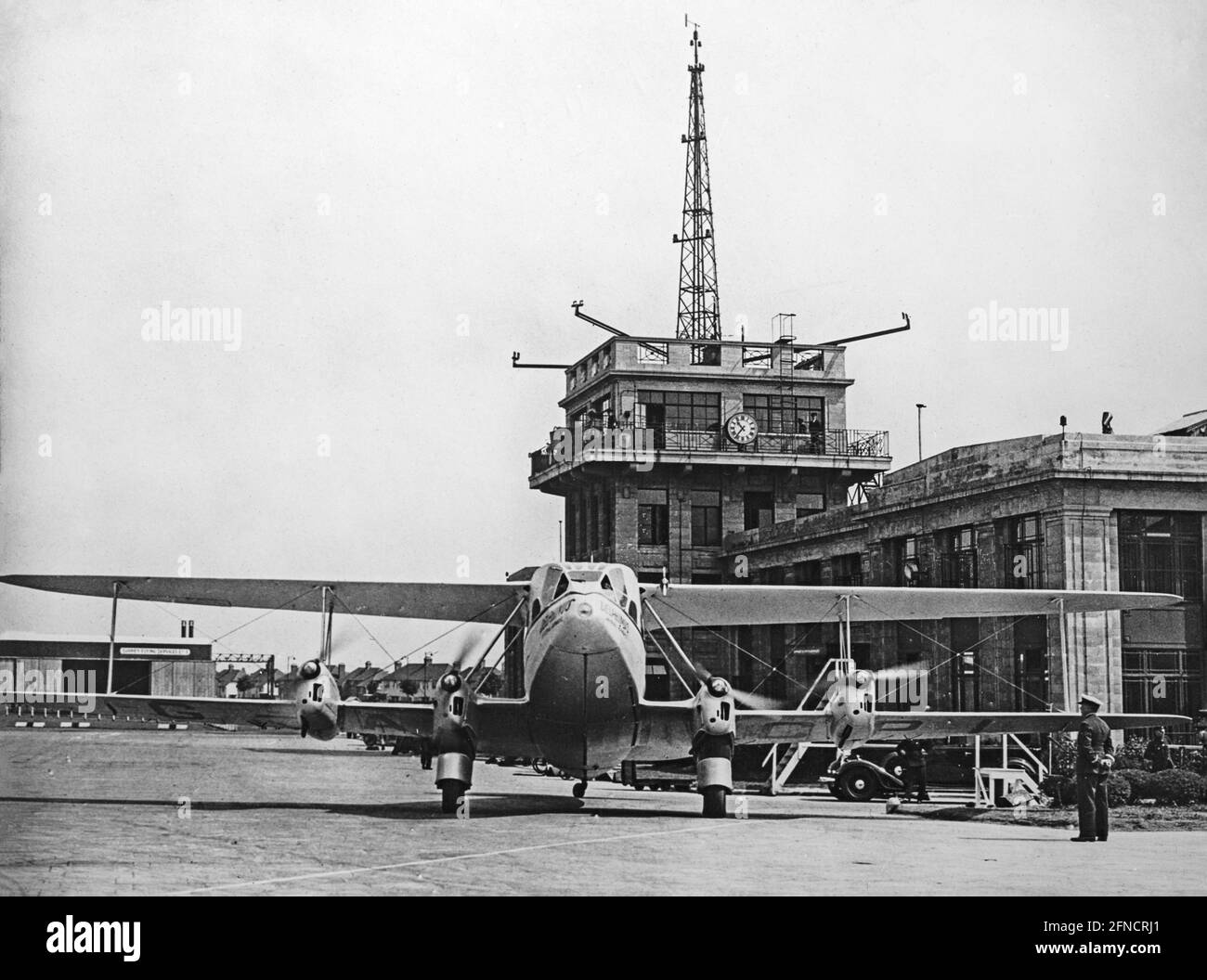 Vintage black and white photograph showing an Imperial Airways De Havilland DH.86 Express, registration G-ACPL and named 'Delphinus', at Croydon Airport, London, in the 1930s. The airport control tower behind. Stock Photo