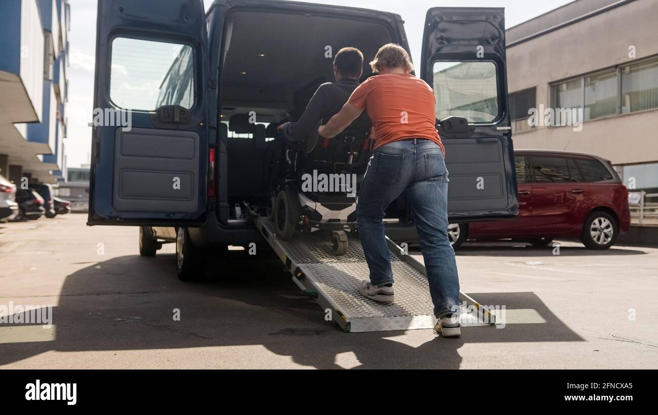 Assistant helping disabled person on wheelchair with transport using