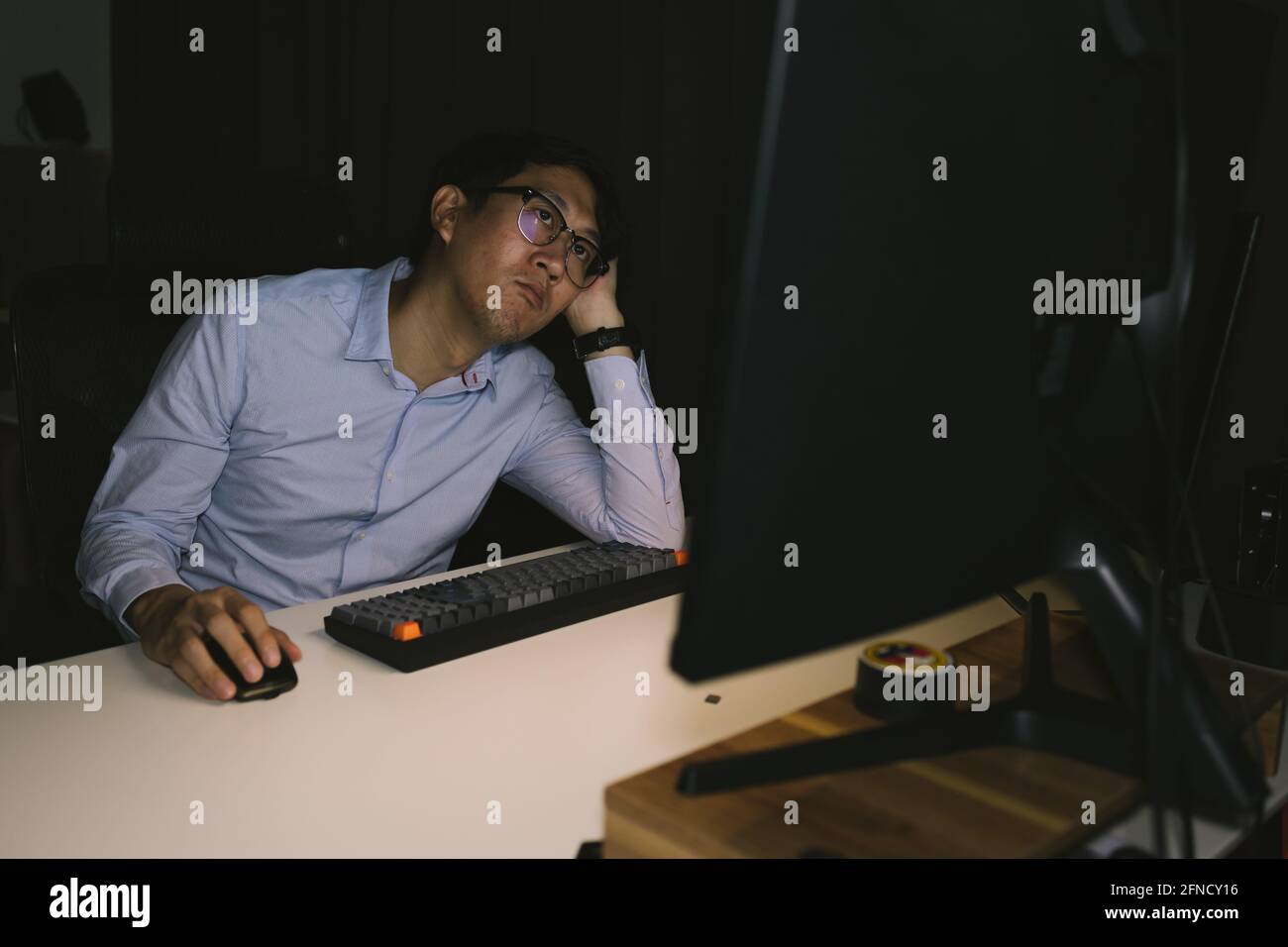 Young Asian businessman working overworked in corporate office. Male office worker thinking and stressing during overtime hours at night Stock Photo