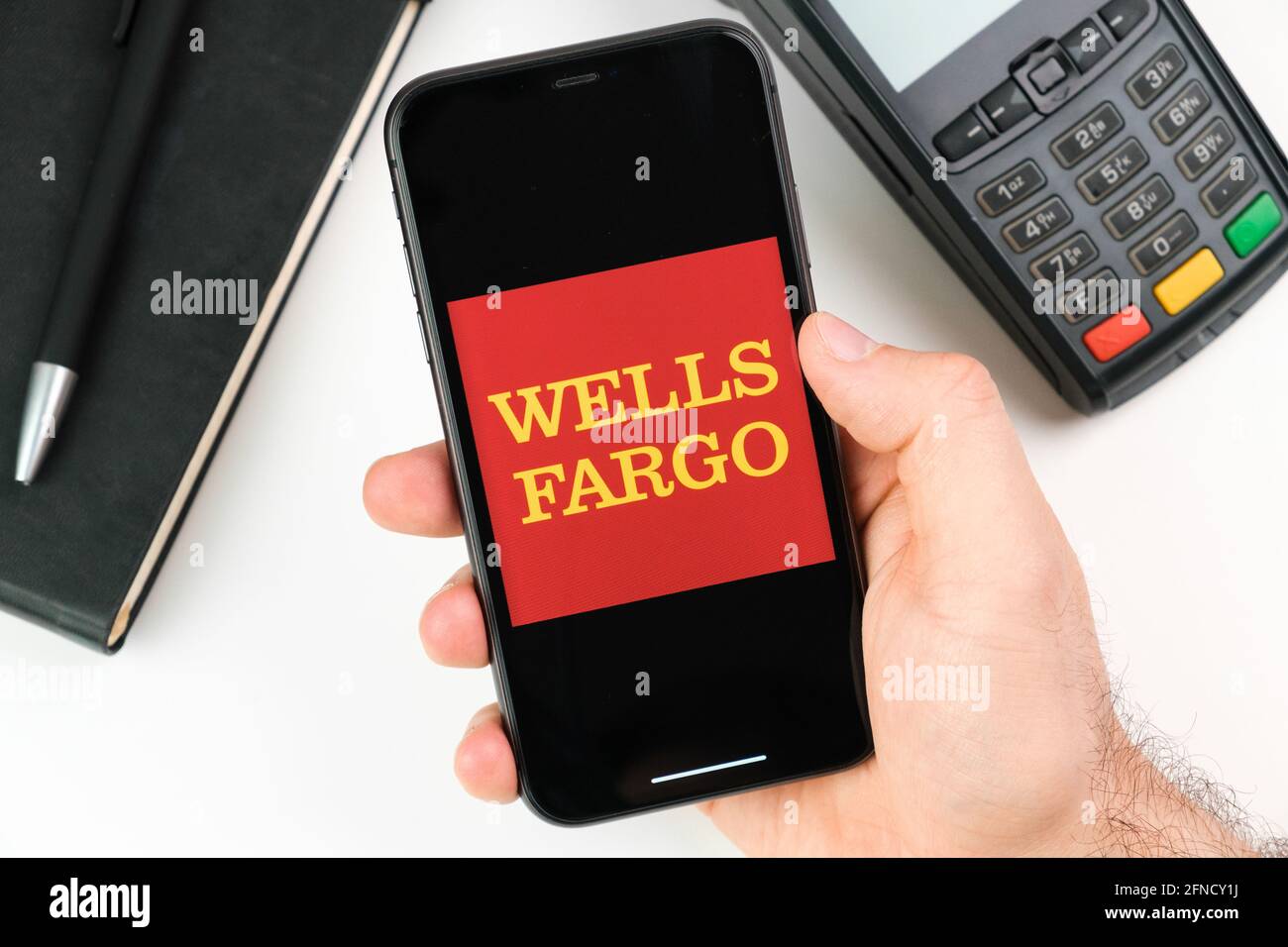 Wells Fargo bank logo on the black smartphone screen in mans hand on the background of payment terminal, May 2021, San Francisco, USA Stock Photo