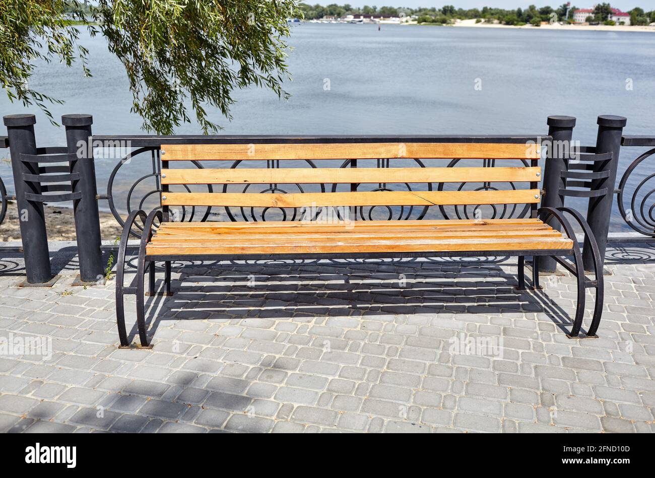 Embankment with bench with view on sea. Park wooden bench on the cobbled sidewalk Stock Photo