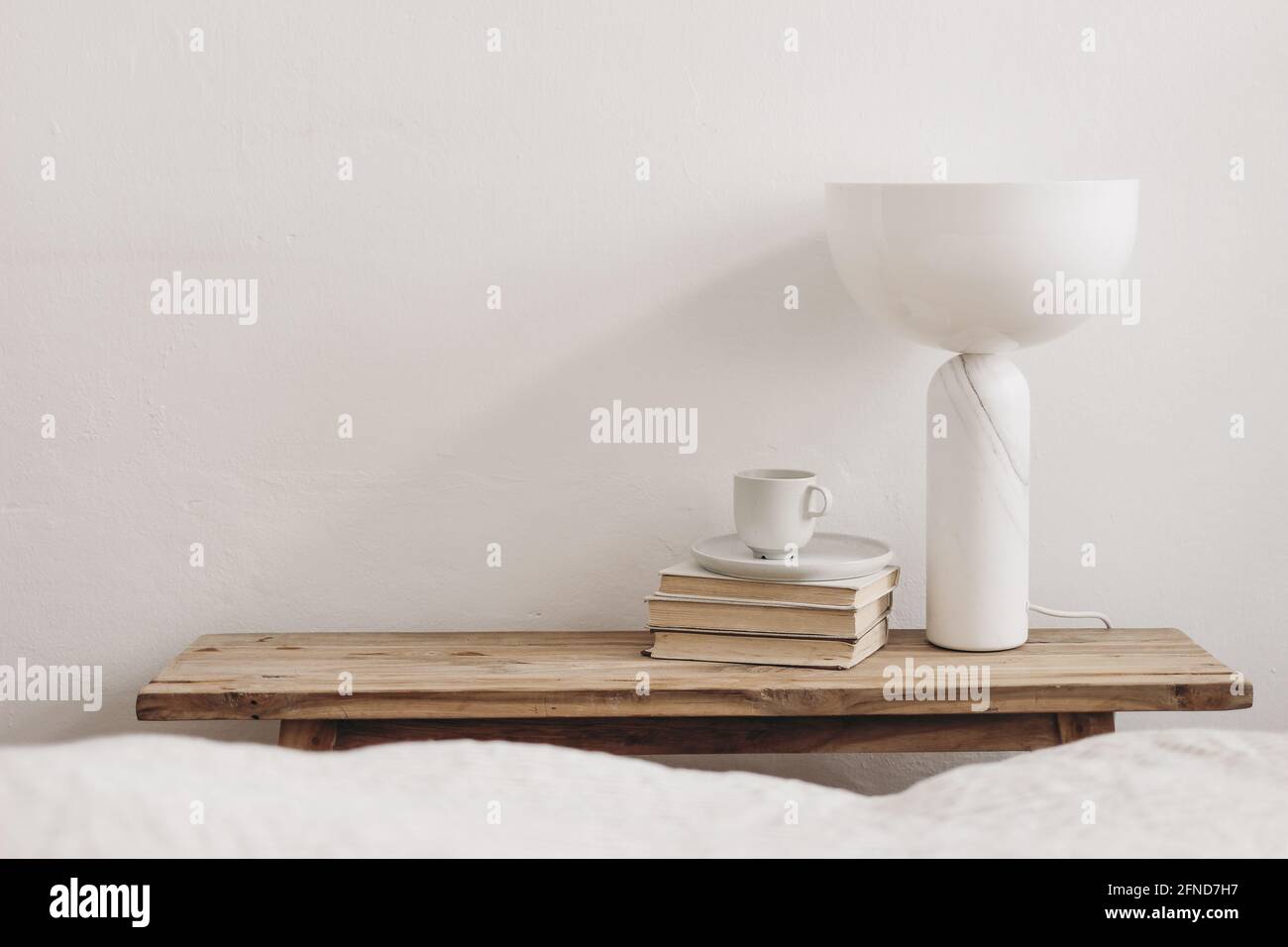 Cup of coffee on pile of books and modern marble geometric lamp. Vintage bench, table. White wall background. Scandinavian interior, bedroom Stock Photo