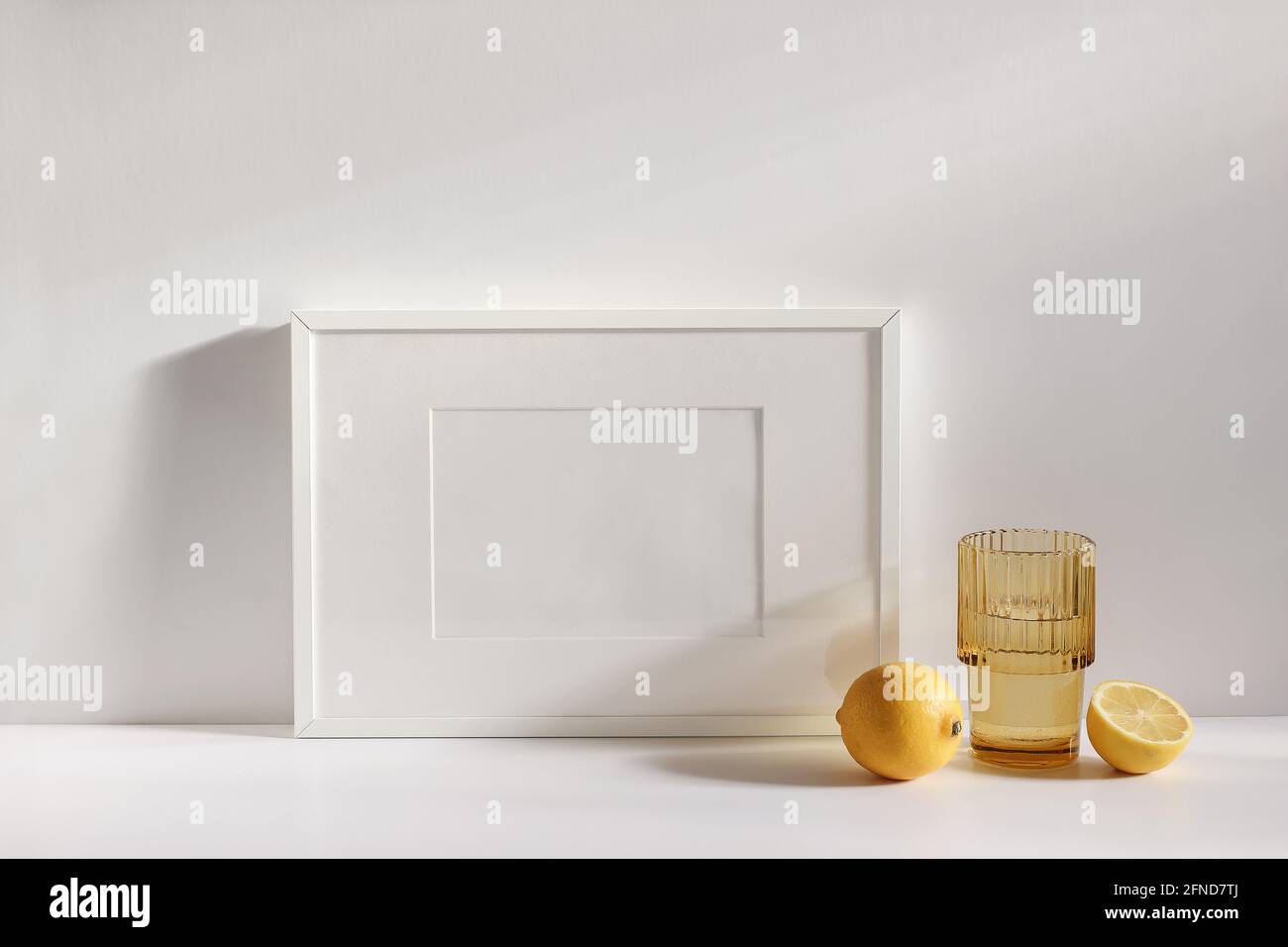 Summer stationery still life scene. Cut lemon fruit. Golden rippled glass of water on beige table background in sunlight. Blank white horizontal Stock Photo