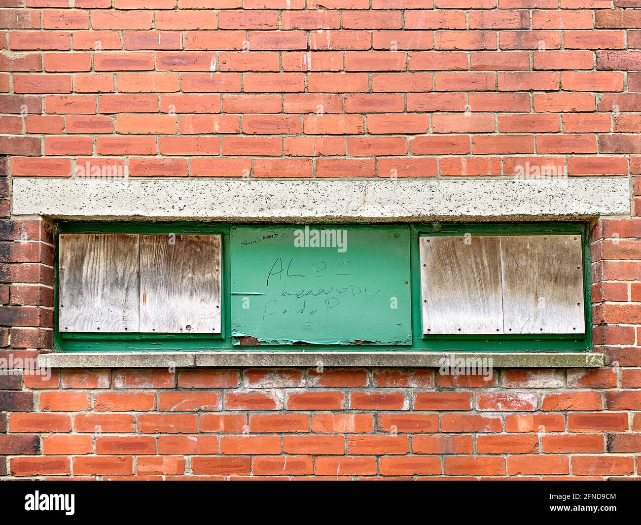Three boarded up windows set in red brick wall Stock Photo