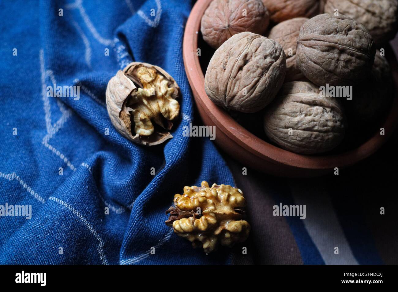 Shelled and cracked walnuts scattered from the bowl on a blue and brown cotton kitchen cloth were photographed in dark mode. Creative concept composit Stock Photo