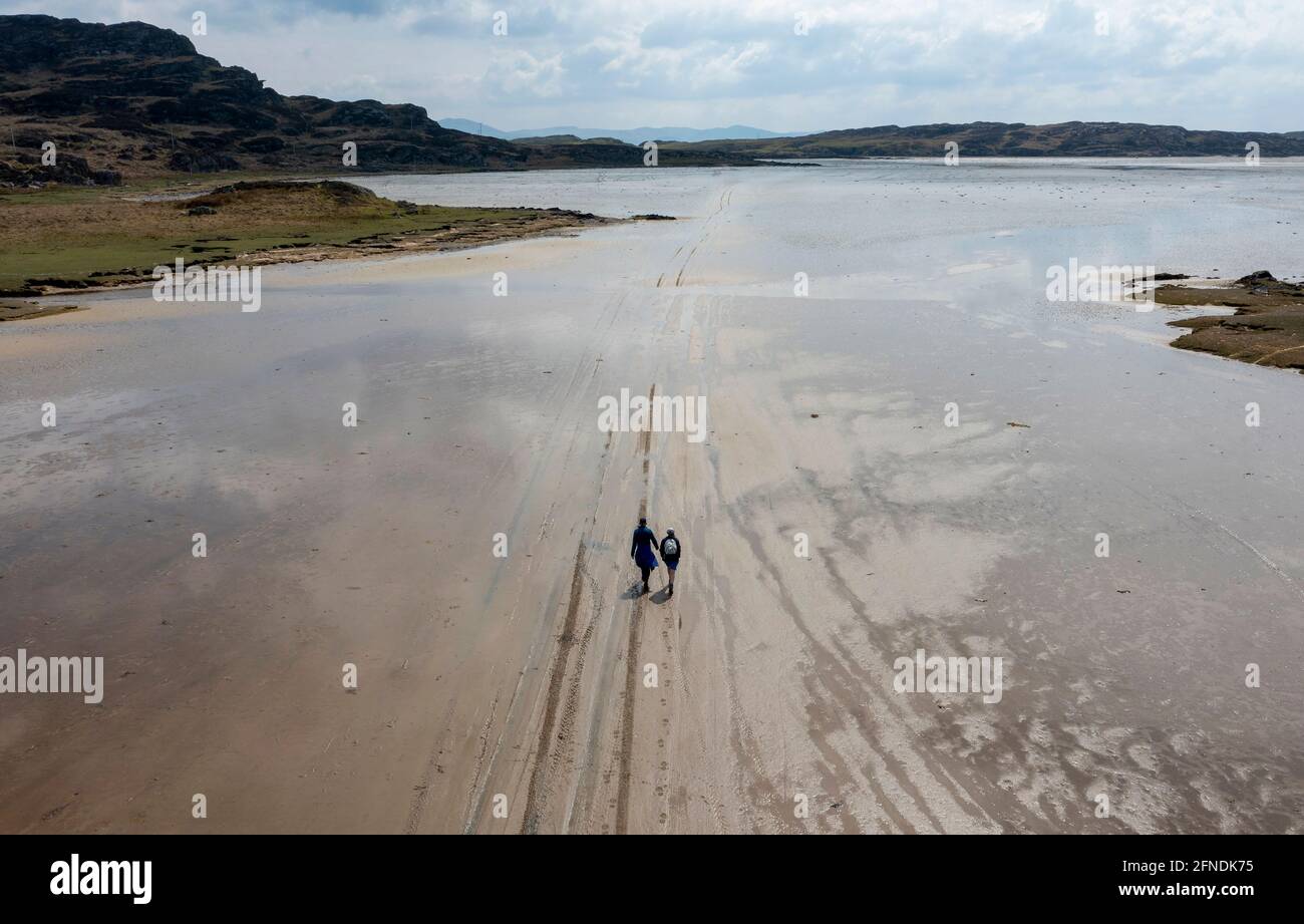 Two walkers follow tyre tracks in the sand leading to the tidal island of Oronsay, The Strand Isle of Colonsay, Scotland, UK Stock Photo