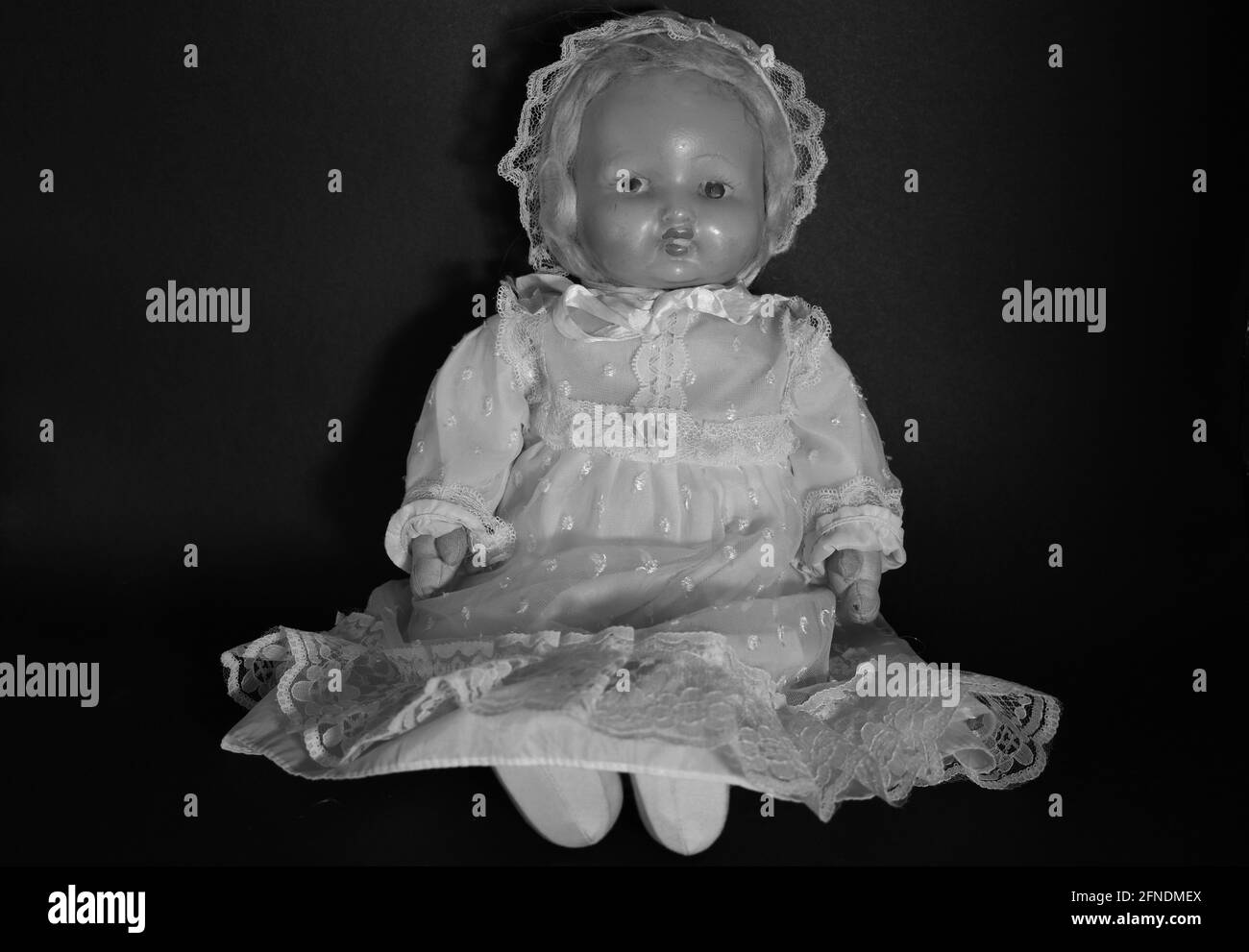 A grayscale of a creepy old doll sitting in the darkness Stock Photo