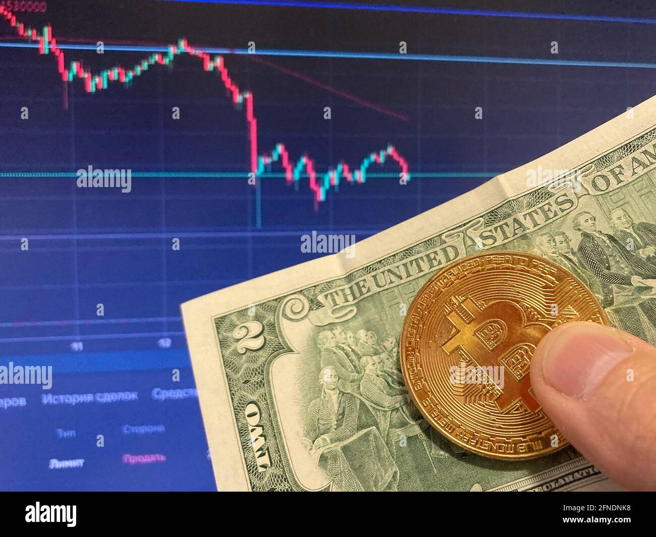 Bitcoin coin on paper bill two Dollars, USD - blurred background. The electronic schedule of bitcoin, volume trades Stock Photo