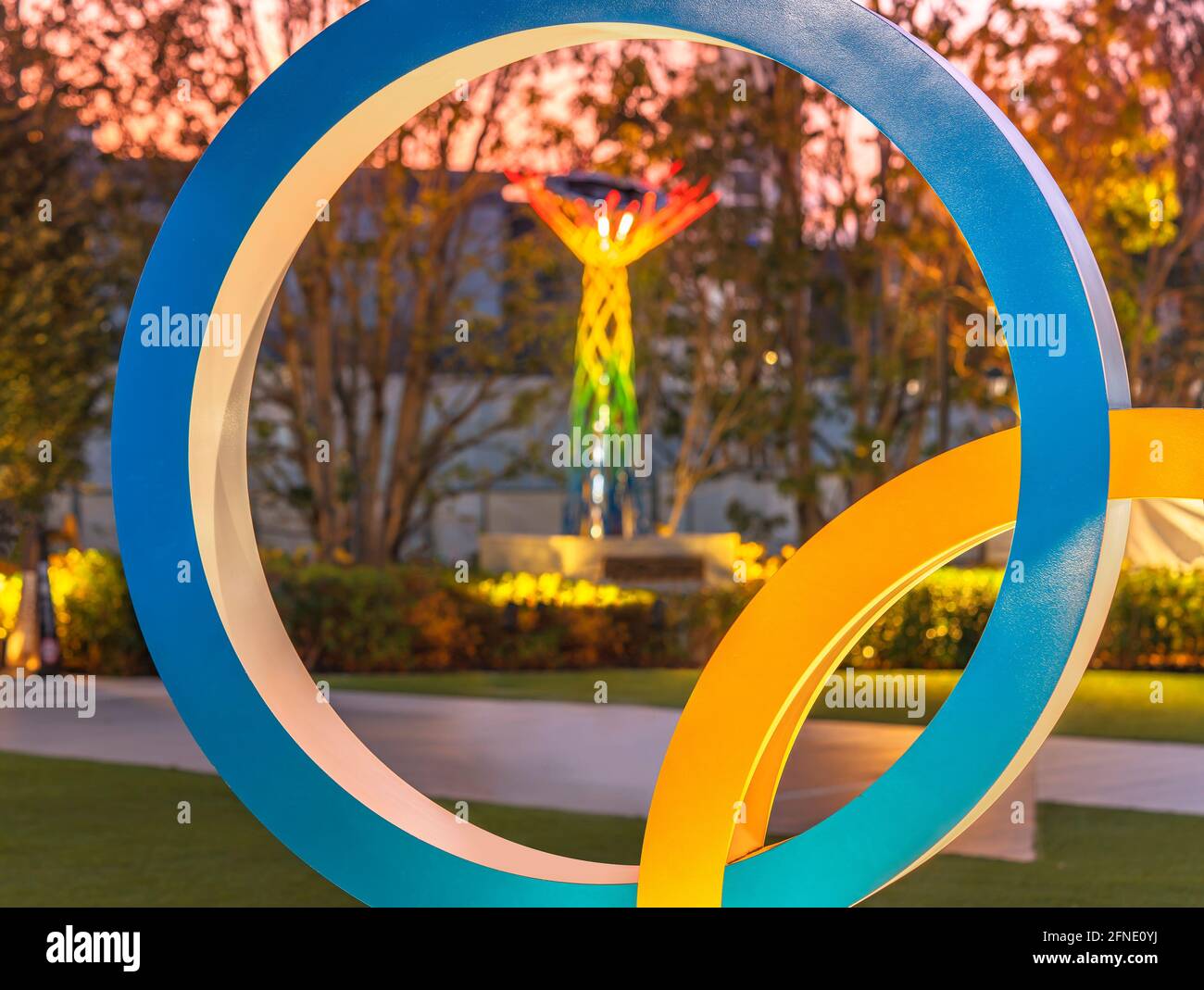 tokyo, japan - may 10 2021: Close up on one of ring of the Olympic Rings monument lighted up at dusk with the illuminated Olympic Cauldron of Nagano O Stock Photo