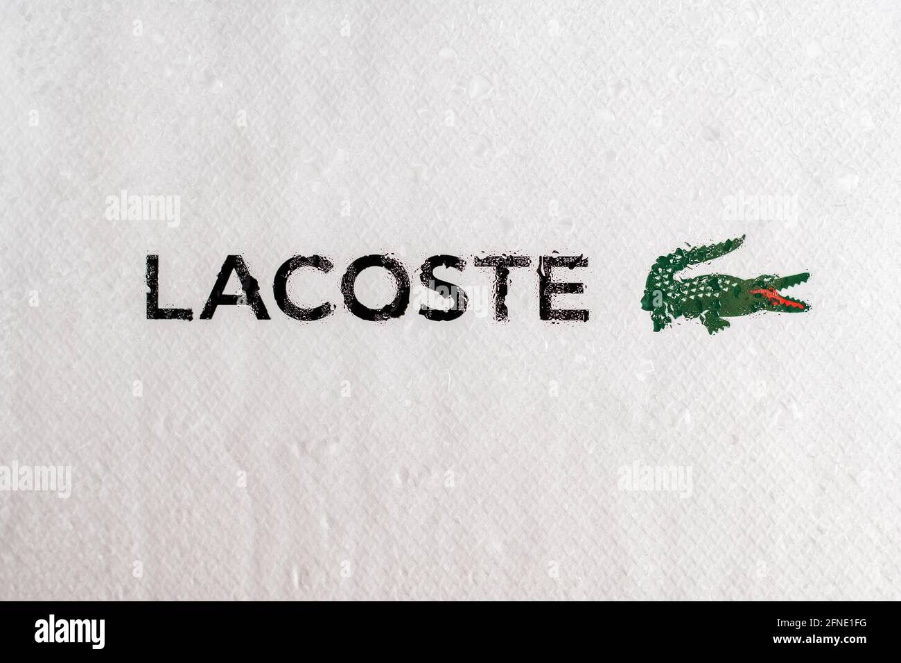 Minsk, Belarus 07.05.2021: Lacoste logo and name behind glass, on white background with water drops. Stock Photo