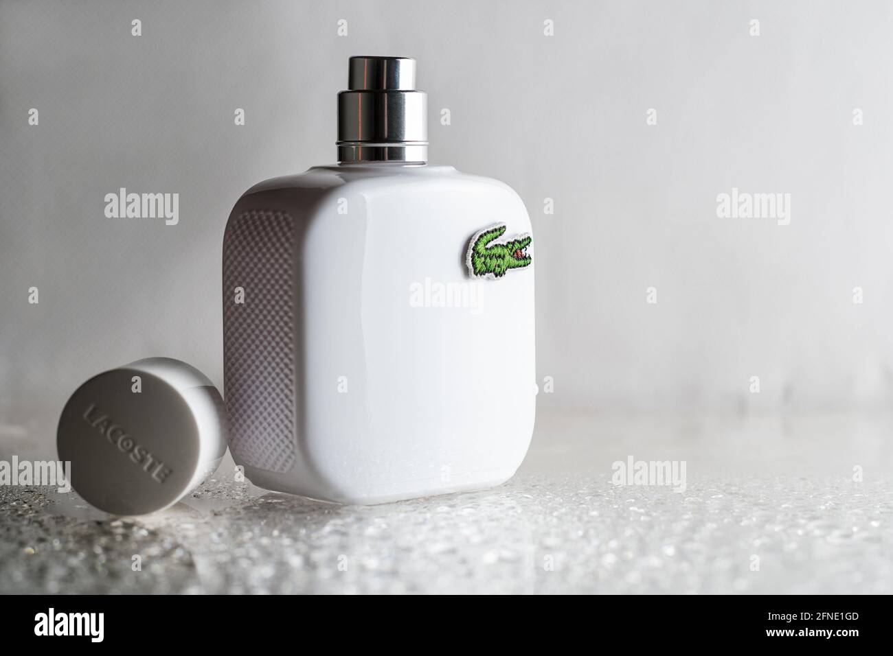 Minsk, Belarus 07.05.2021: White open perfume bottle with Lacoste logo on wet surface, with drops on white background Stock Photo
