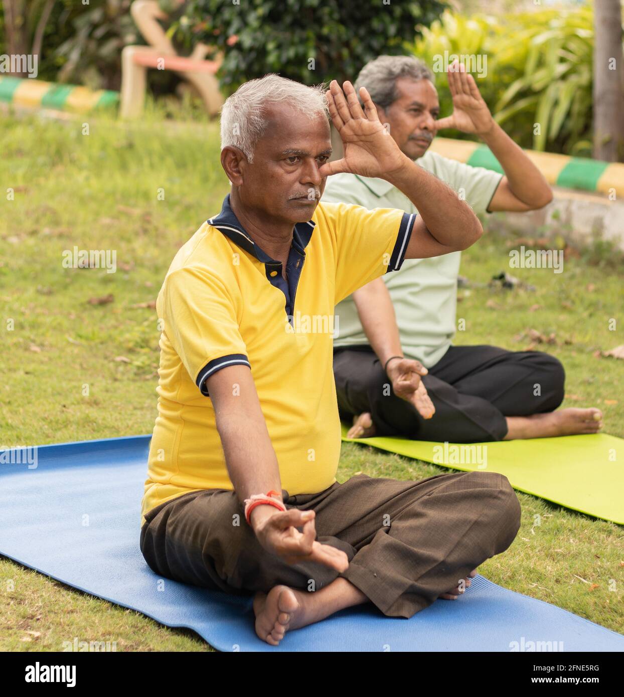 Two senior man doing alternate Nostril Breathing exercise or nadi shodhana pranayama at park on yoga mat at park - Concept of healthy active old Stock Photo