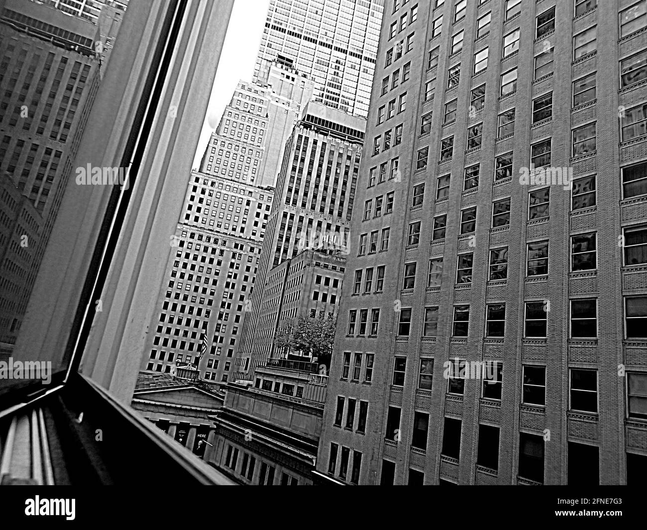 View with window reflection above Broad St and NYSE in Manhattan financial district. High density black and white build environment with one tree. Stock Photo