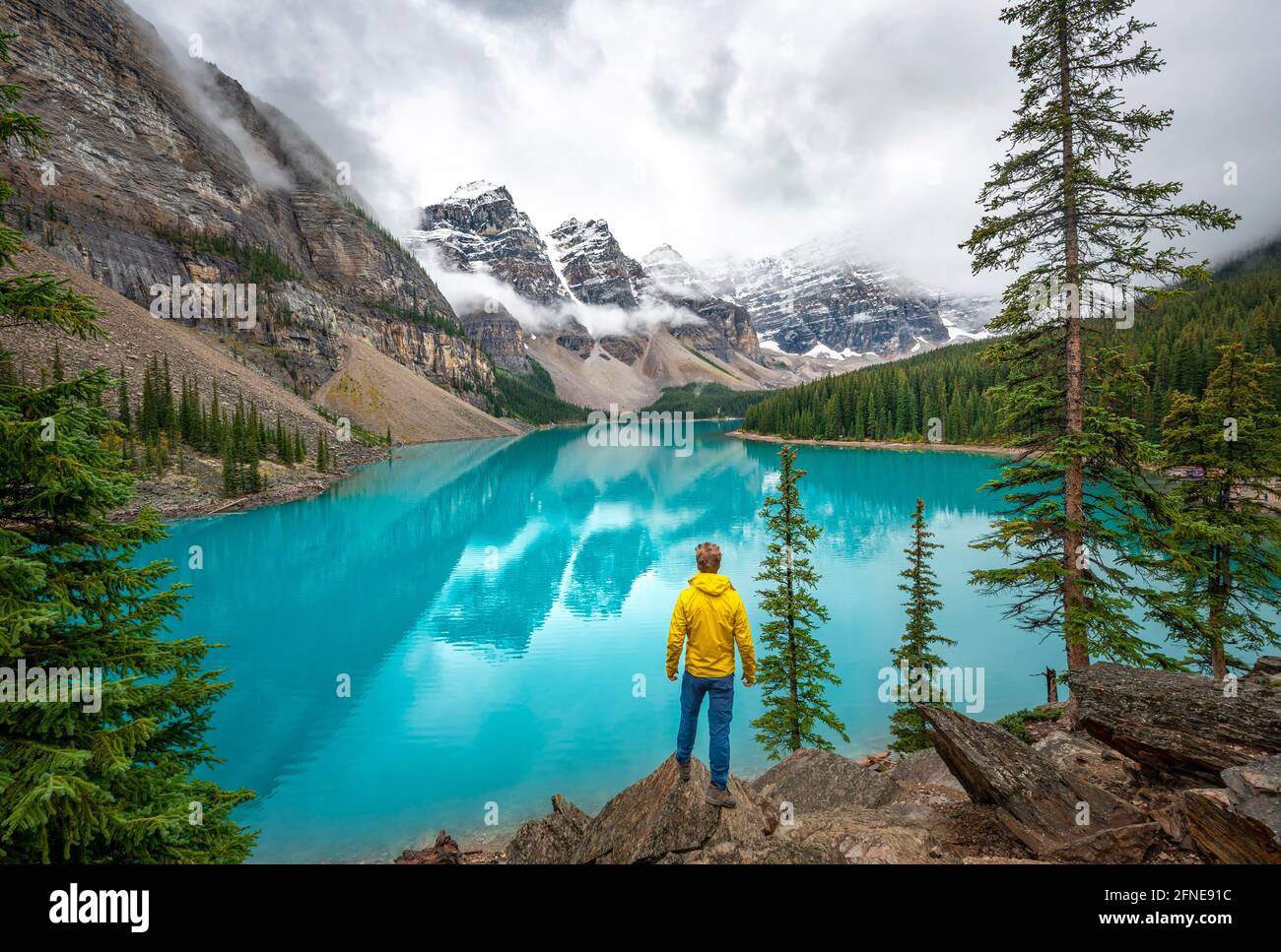 Young man looking at mountains, cloudy mountain peaks, reflection in ...