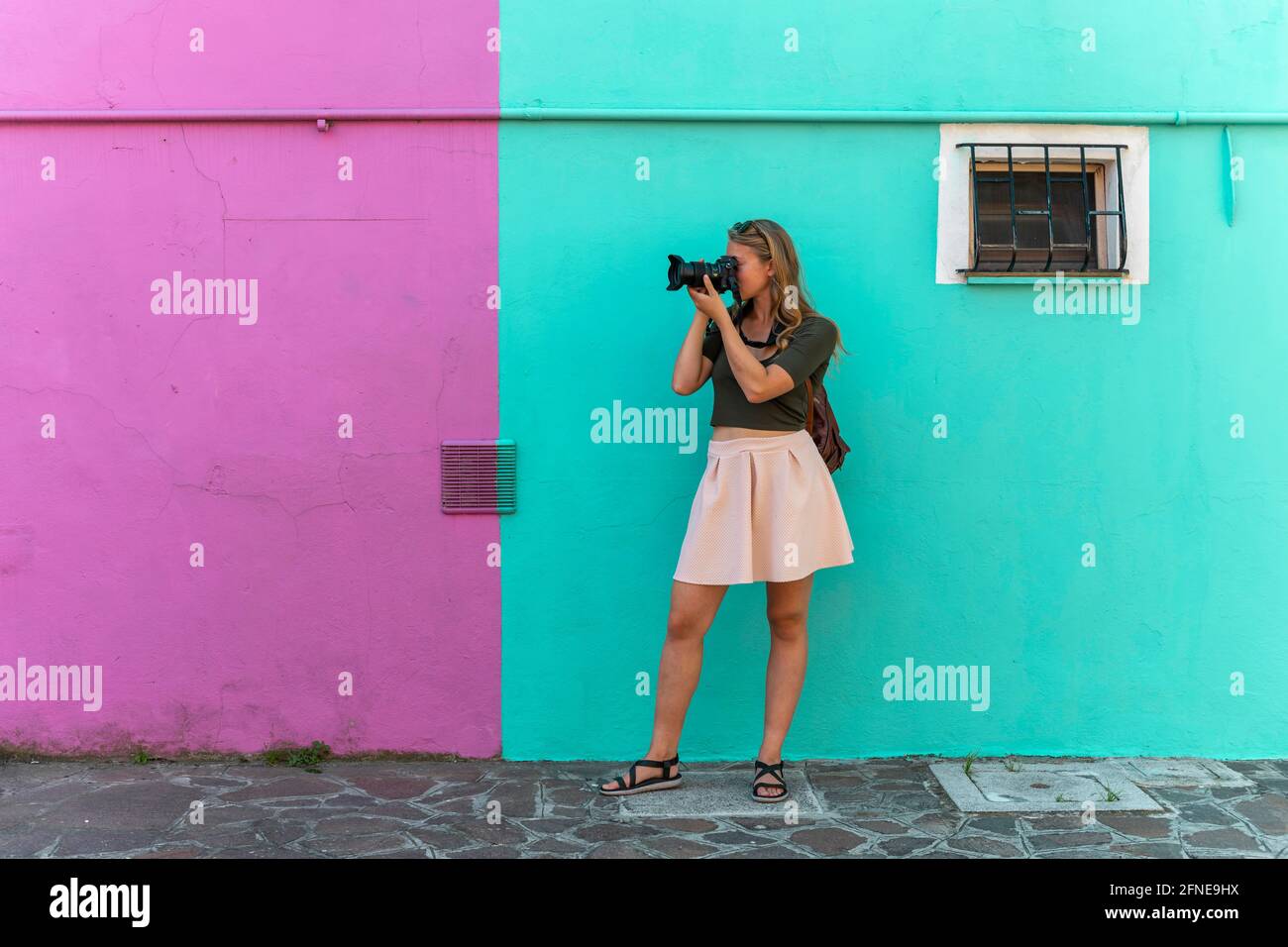 Young woman in front of colorful house, pink and turquoise house facade, tourist photographed on Burano Island, Venice, Veneto, Italy Stock Photo