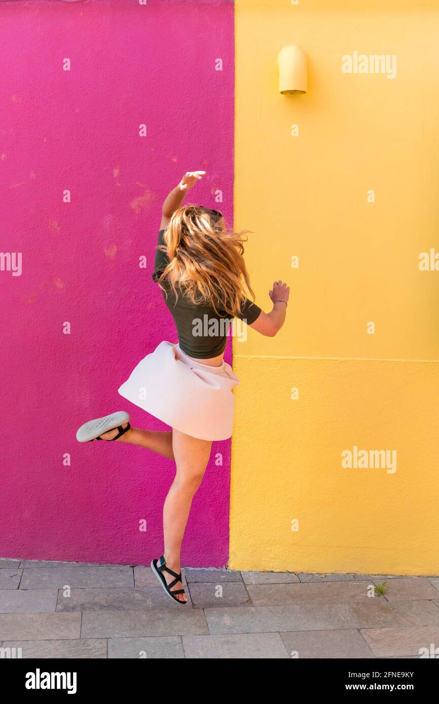 Young woman in dress jumps happily in front of colorful house, yellow and pink house facade, Burano Island, Venice, Veneto, Italy Stock Photo