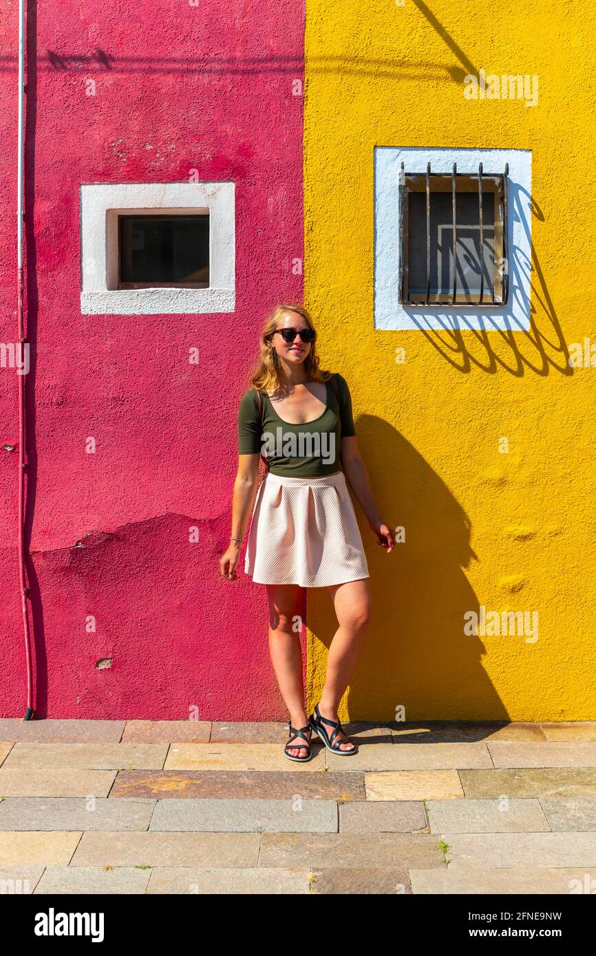 Young woman in front of colorful house, red and yellow house facade, Burano Island, Venice, Veneto, Italy Stock Photo