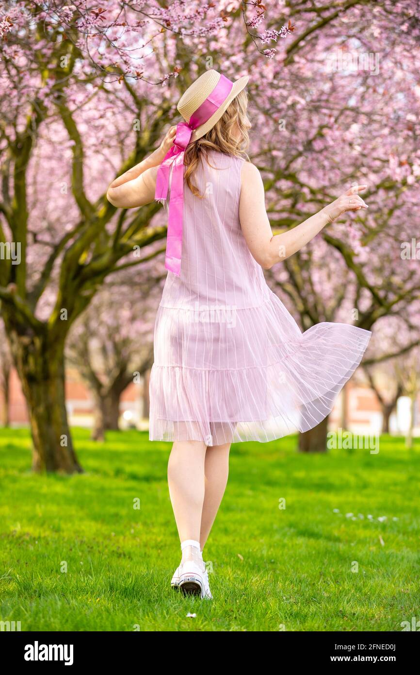 Beautiful woman in straw hat walking in a spring garden with blooming ...