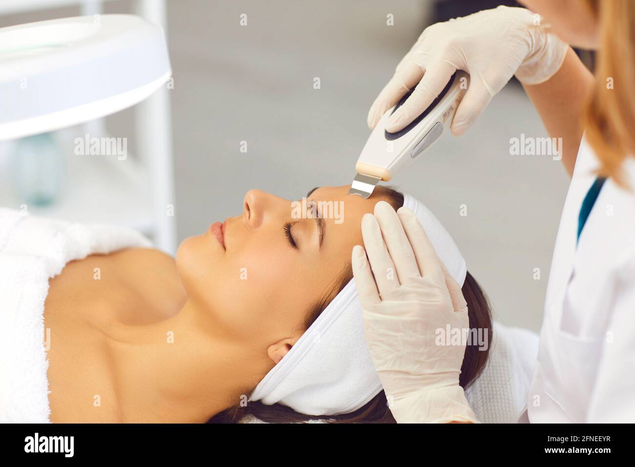 Hands of cosmetologist making professional ultrasound apparatus facial cleaning for woman Stock Photo