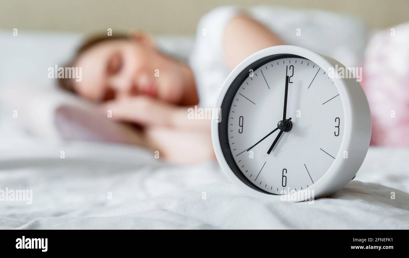 Happy young woman sleeping near bed side alarm clock. Calm healthy morning sleep of woman in pajamas. Morning routine and wake up from alarm clock Stock Photo
