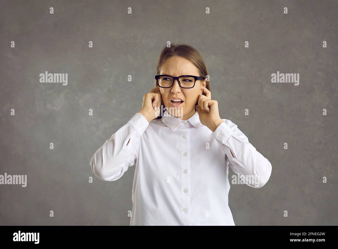 Woman who is irritated by a loud noise closes her ears, not wanting to hear anything. Stock Photo