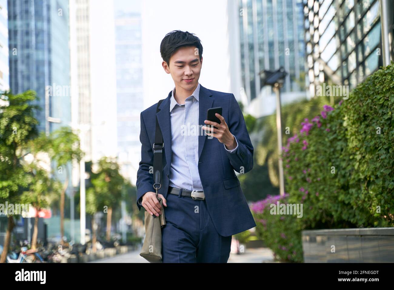 young asian businessman looking at messages on cellphone while walking in the street in downtown of modern city Stock Photo