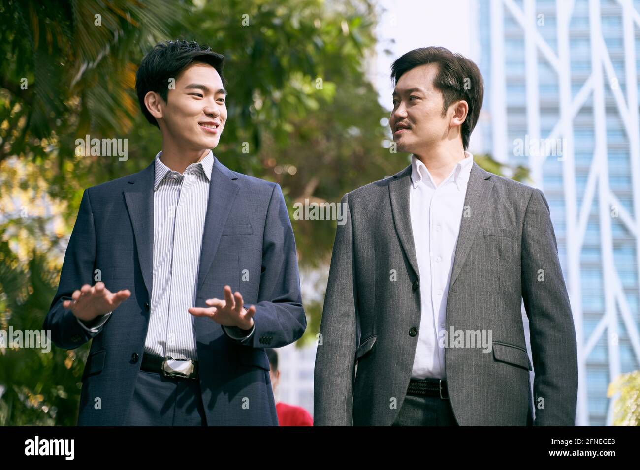 two asian business people walking talking on street in modern city Stock Photo