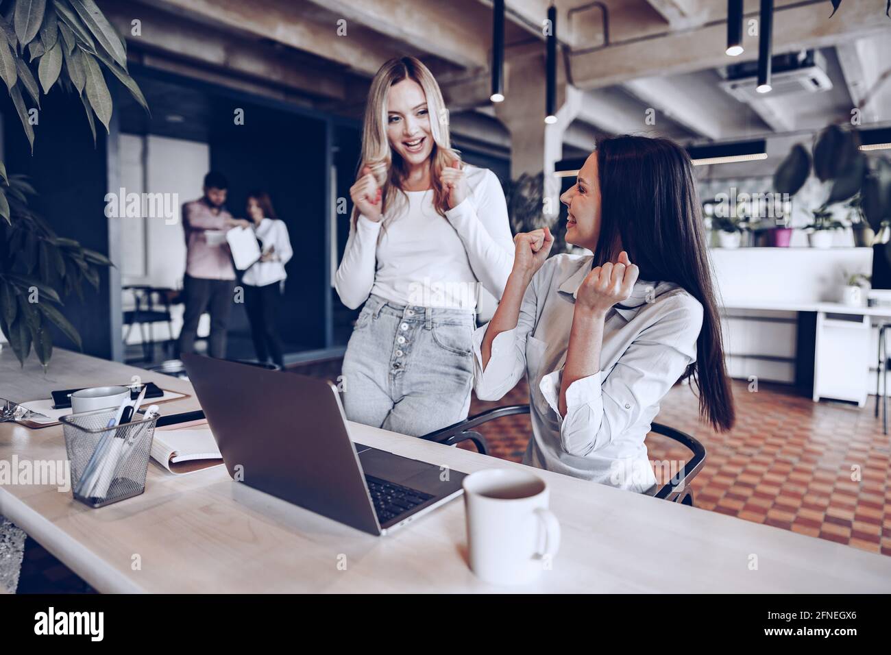 Two young happy businesswomen celebrating project success in office ...
