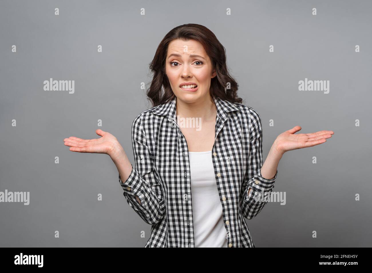 A confused woman stands uncertainly, shrugs her shoulders, can't give an answer to a difficult question, has a confused expression on her face. Stock Photo