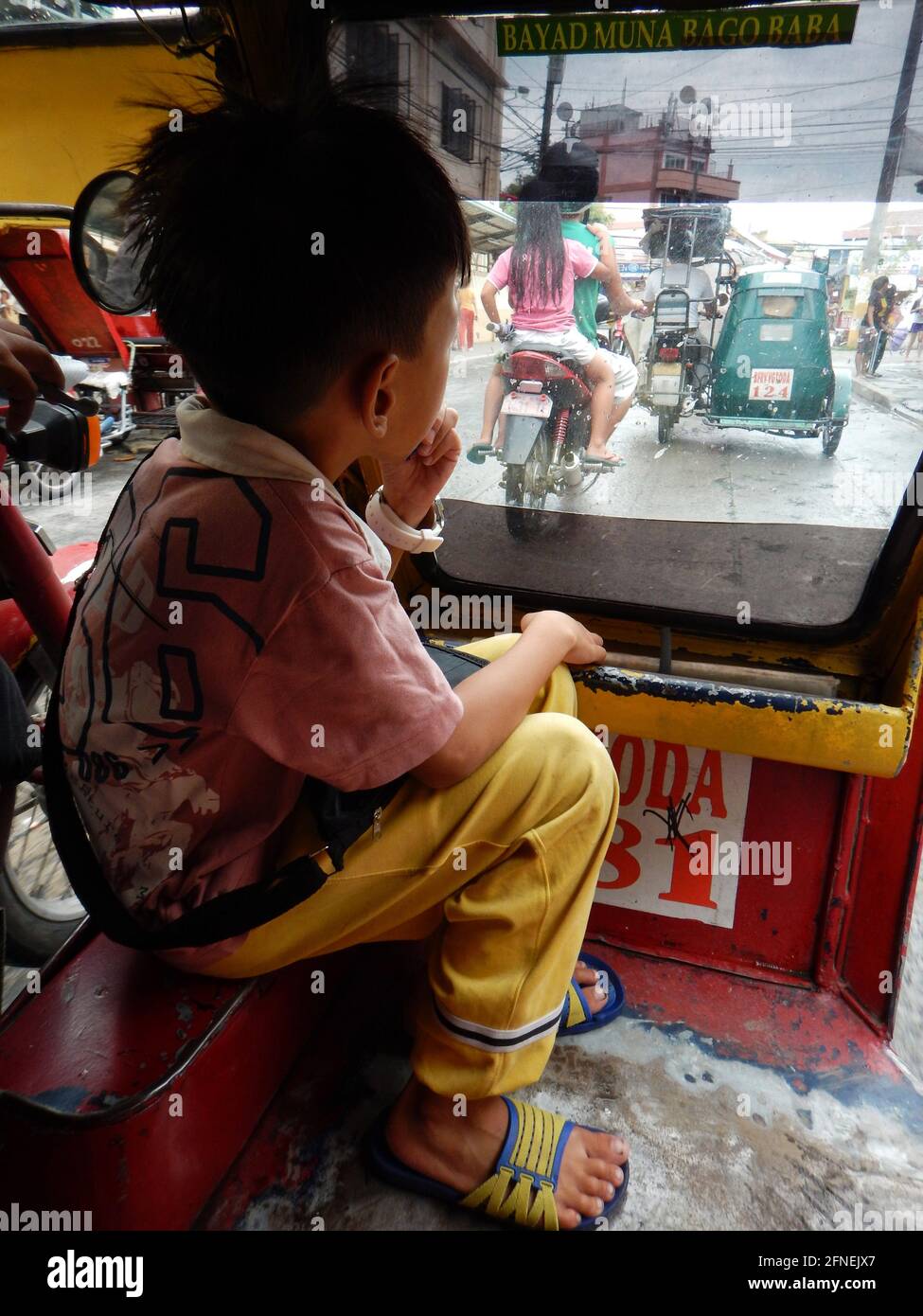 Small boy riding in a pedicab, looking through the window at other traffic in Novaliches, Manila, Philippines Stock Photo