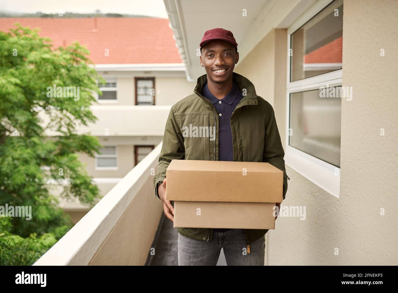 Smiling African delivery man standing outside carrying packages Stock Photo