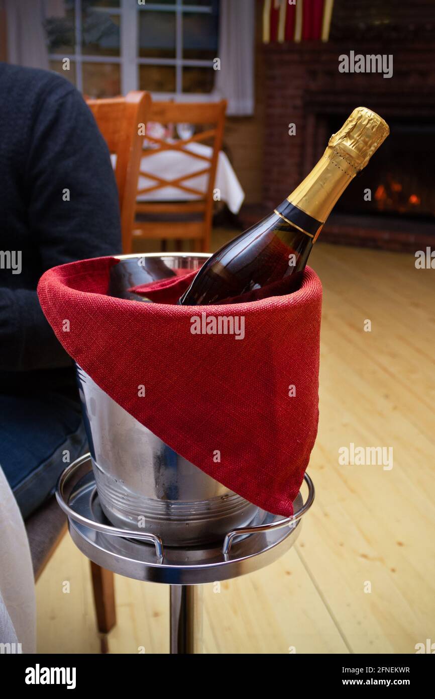 Bottle of champagne in metal ice bucket with red towel on stand in interior of restaurant. Stock Photo