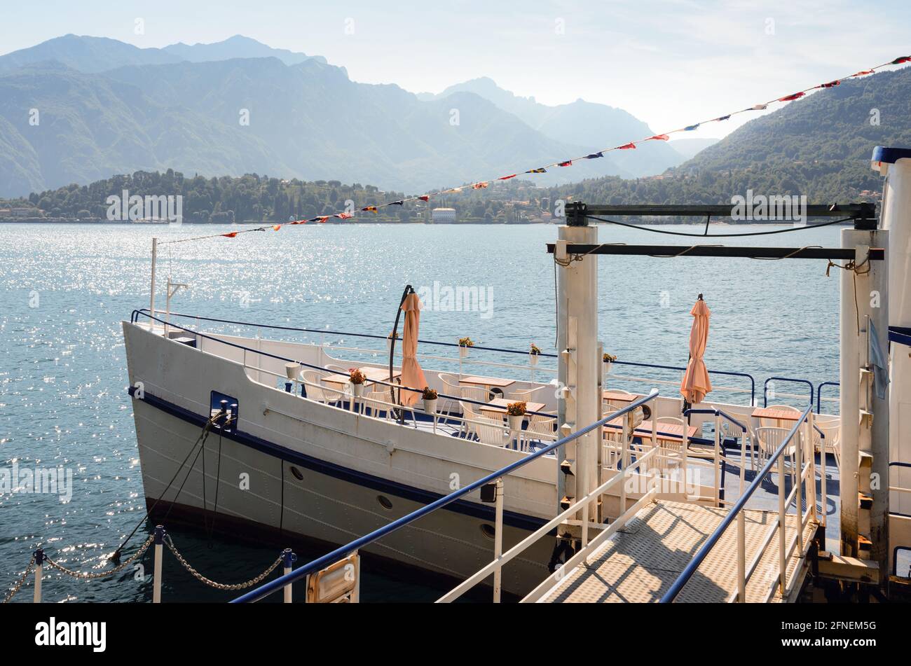 Early morning view of the Como Lake with a restaurant ship docked in Tremezzo, Italy, clear sky with fog, soft sunlight and mountains in the distance Stock Photo