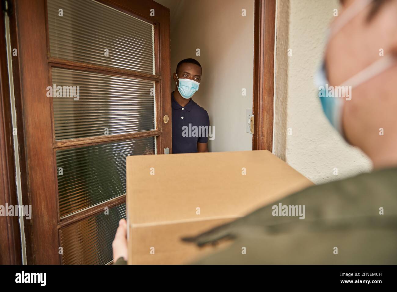 African man in a mask receiving a courier package at home Stock Photo