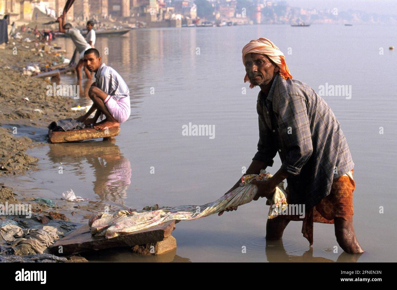 Dhobi wallahs on the banks of the Ganges in Varanasi. Long before the morning dawns, the dull thumping of the washers can already be heard from the dhobi ghats on the Ganges. The method is simple but successful. The cloth is soaped and repeatedly beaten on a flat stone until the dirt comes off. It is mostly casteless people who do this very strenuous work. Professional washing is a male domain in India, as it requires great physical endurance. [automated translation] Stock Photo