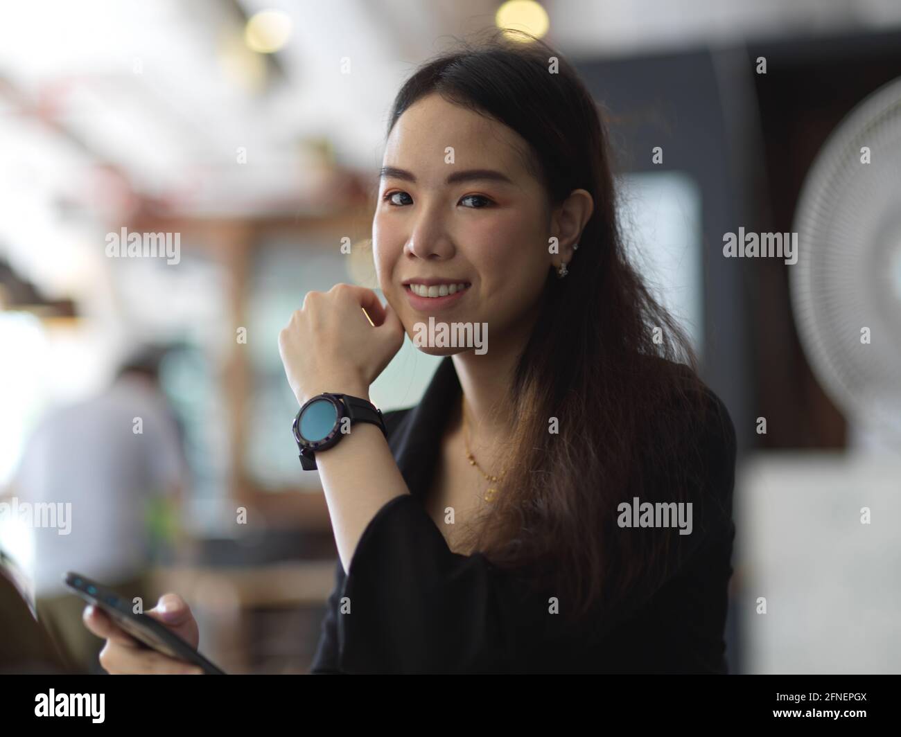 Portrait of young businesswoman in black suit wearing smartwatch, smiling and looking into camera Stock Photo