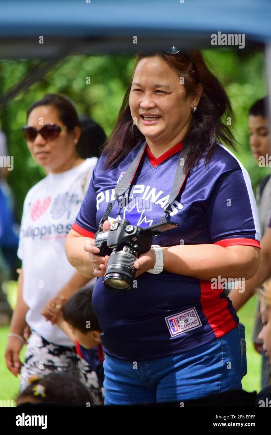 Asian Filipino woman taking pictures with a DSLR during Philippines Independence day 2015, Vincent Massey Park, Ottawa, Ontario, Canada Stock Photo